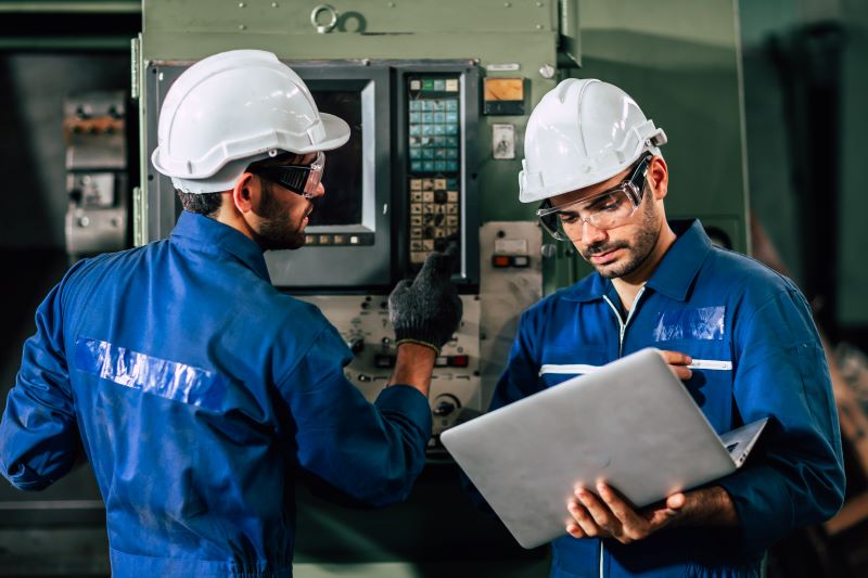 Inversor de frequência: engenheiros operando máquina industrial e utilizando notebook.