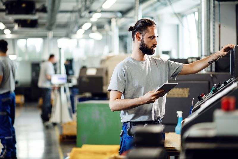 Técnico de manutenção usando sistemas de monitoramento em seu tablet para verificar máquina industrial.