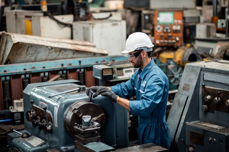 Trabalhador utilizando EPIs mexendo em máquina industrial com eixo, fazendo modificações de acordo com tabela de chavetas.