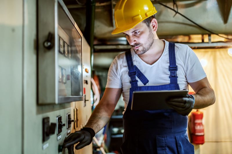 O que é eficiência energética: trabalhador da indústria verificando máquina industrial com tablet na mão.